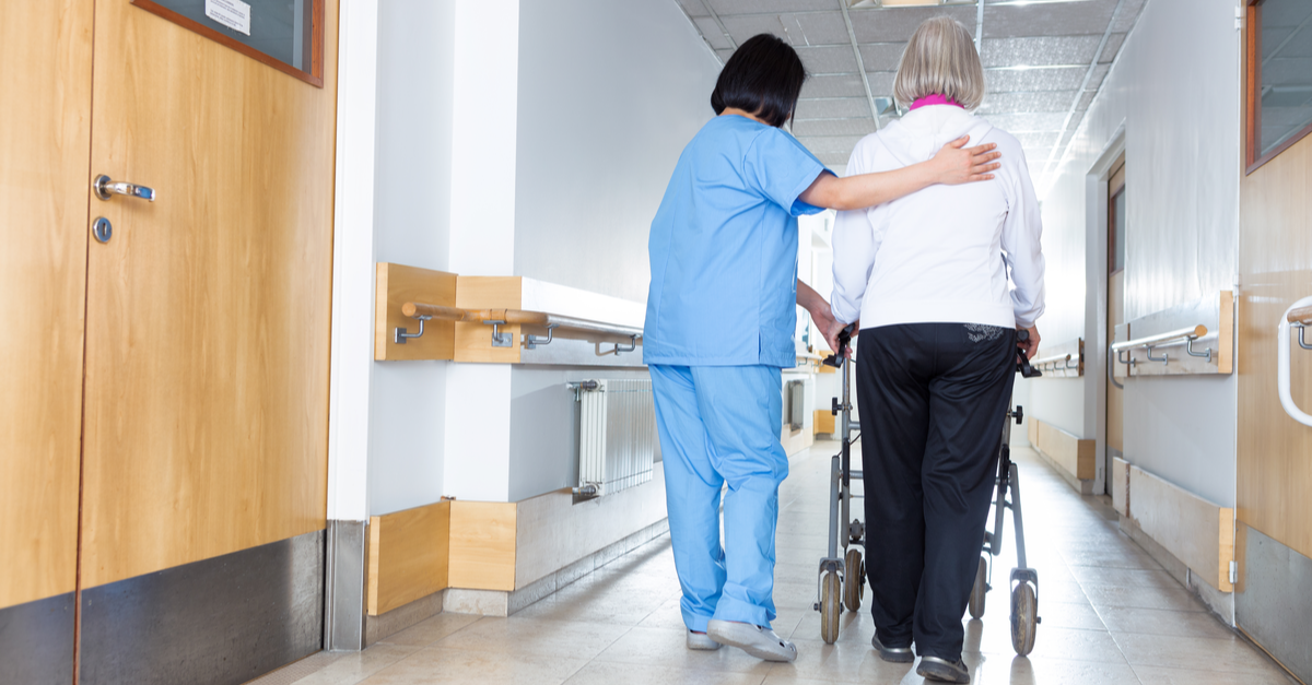 nurse walking an older lady down hallway with walker