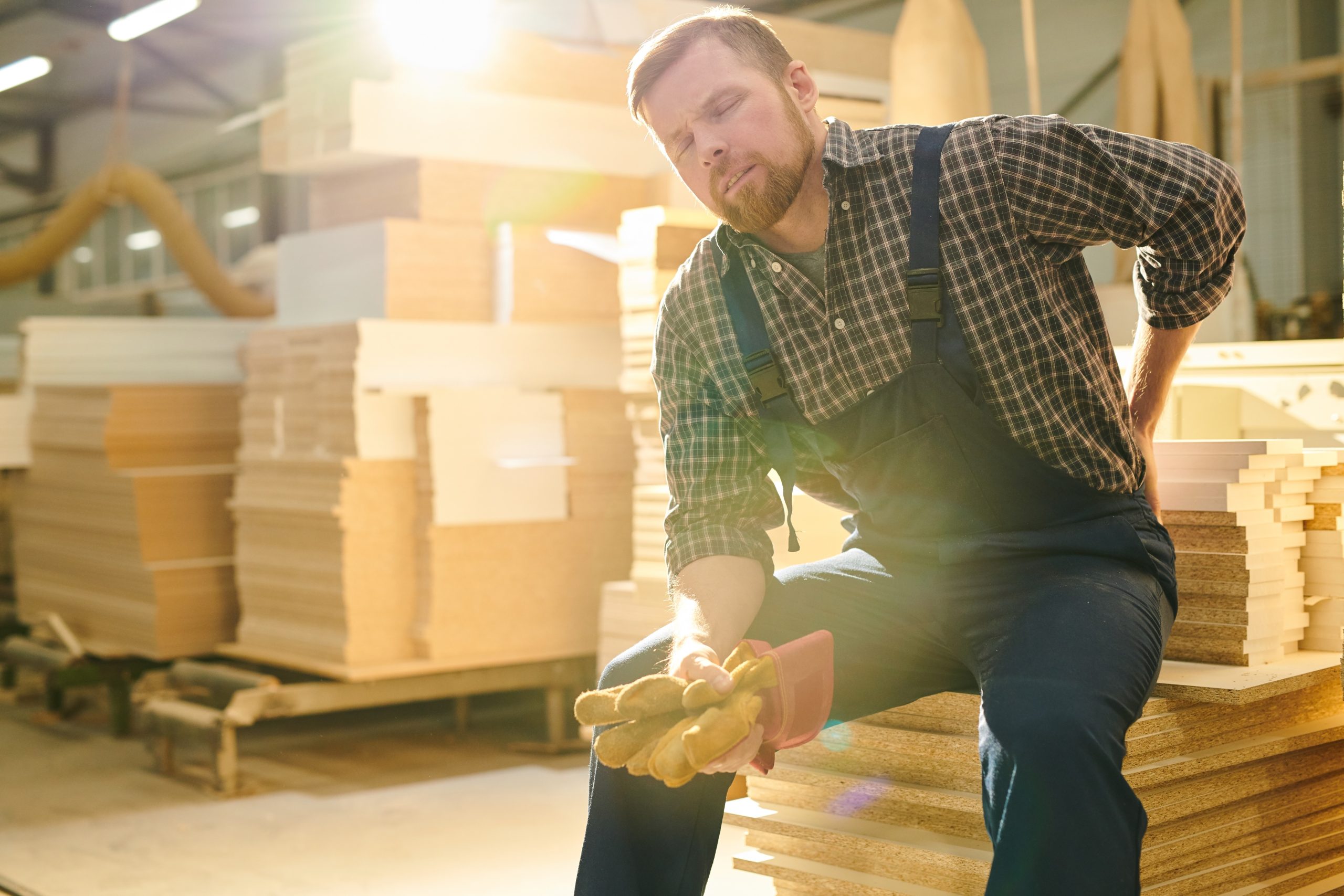 man holding his back in pain in woodshop